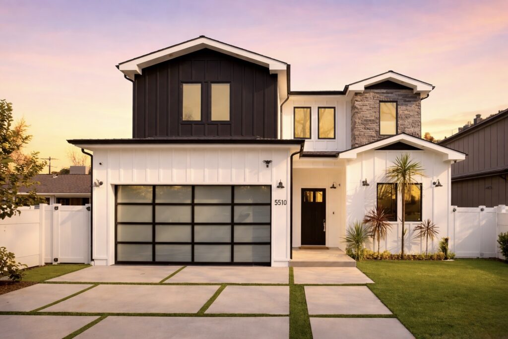 Modern two-story house with glass garage doors and stone accents at sunset.