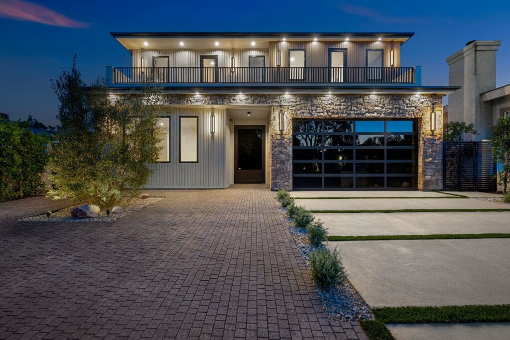 Modern two-story house with stone facade and sleek garage door at dusk.
